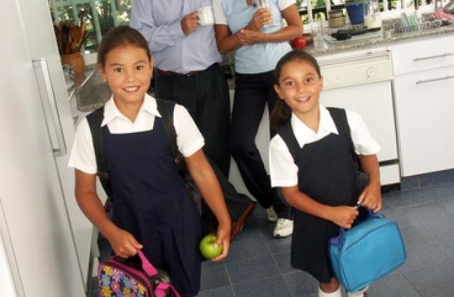 Children in school uniforms ready for school standing in front of parents