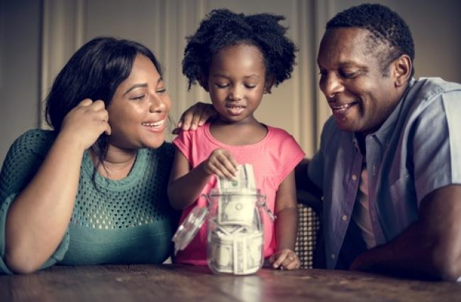 Mother and father admiring child putting money in a savings jar