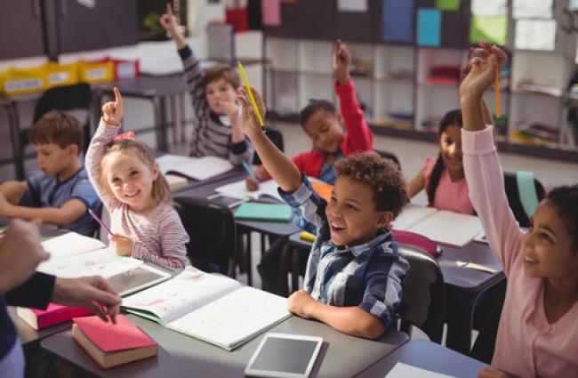 Children in a classroom raising their hands to answer a question