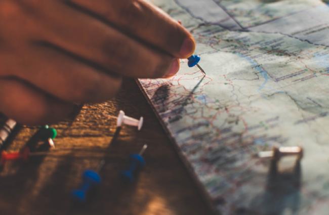 Close up hands putting pins to destination on world map.