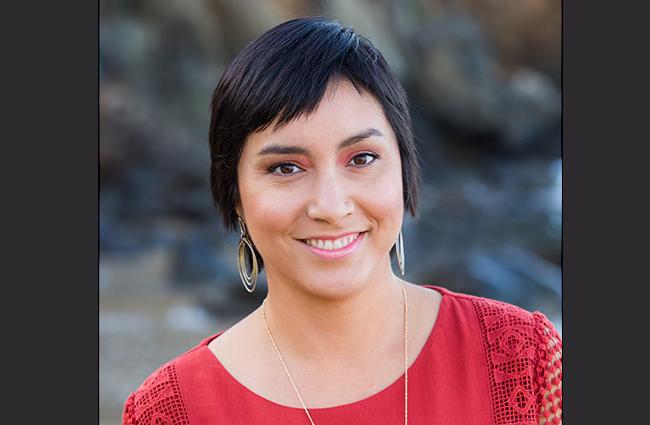 Smiling woman with short black hair, dangling ears, a thin necklace, and a red top