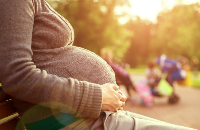 Pregnant person wearing a brownish-grey top with their arms wrapped around their stomach