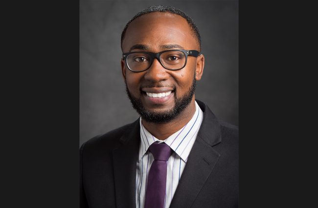 Charles H. Lea III, a smiling Black man with short cropped hair, glasses, and a short beard and mustache. He's wearing a striped dress shirt, dark plum colored tie, and a dark suit jacket.