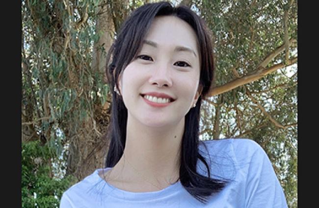 Dr. Ye Ji Kim, a dark-haired Korean American female-identifying epidemiologist wearing a light blue top and standing in front of a tree