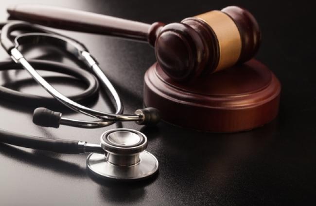 Silver and black stethoscope placed next to a wooden gavel 