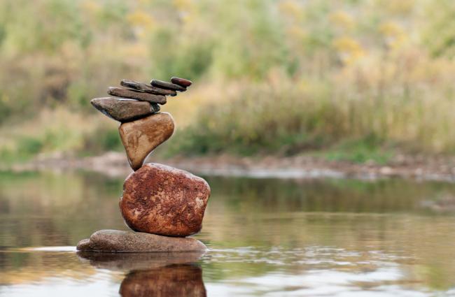 Precarious looking stack of rocks in a lake with grasses in the background.