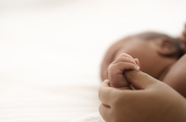 Close up of Black infant holding a Black person's thumb