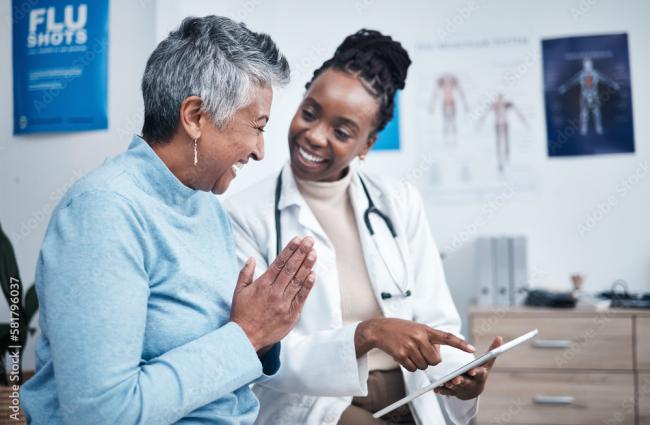 Black doctor smiling and holding a clipboard to help an elderly patient