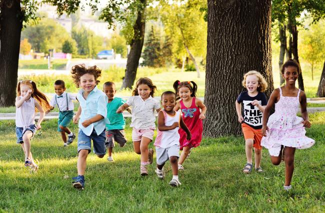 Diverse group of kids running on the grass toward the camera smiling