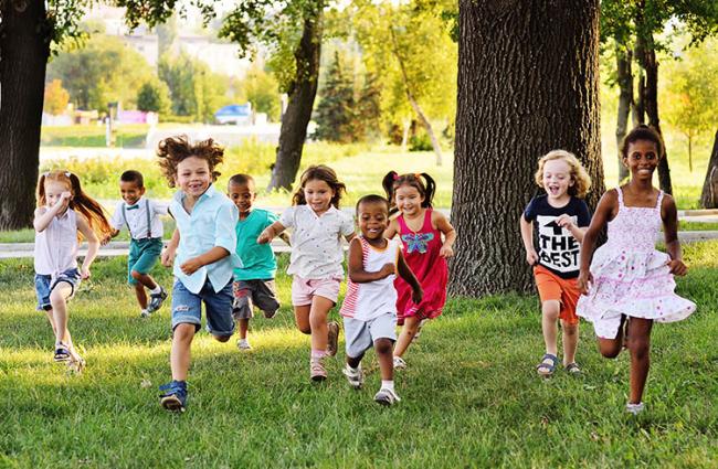 Diverse group of kids running on the grass toward the camera smiling