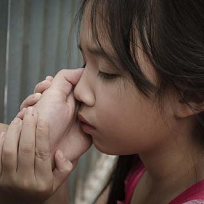 Child with parents hand on their cheek. Parent appears behind bars