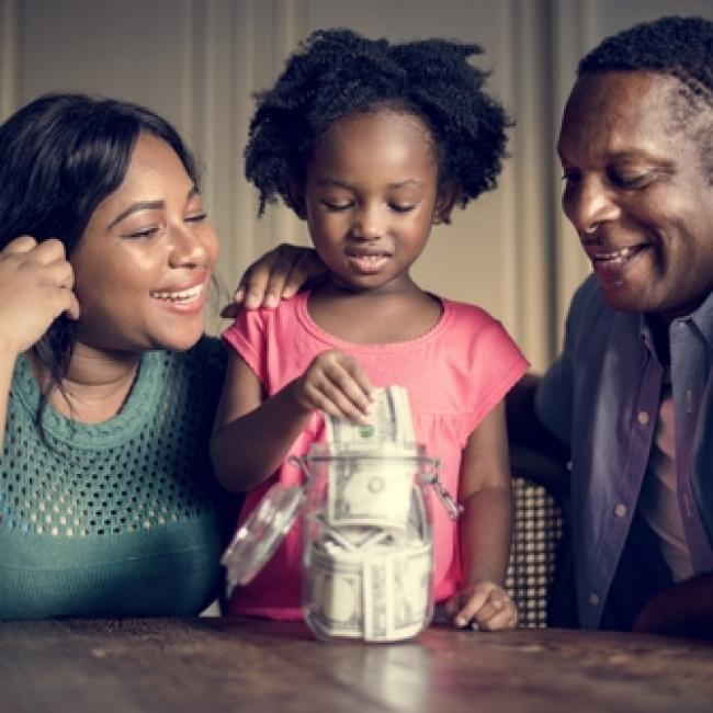 Mother and father admiring child putting money in a savings jar