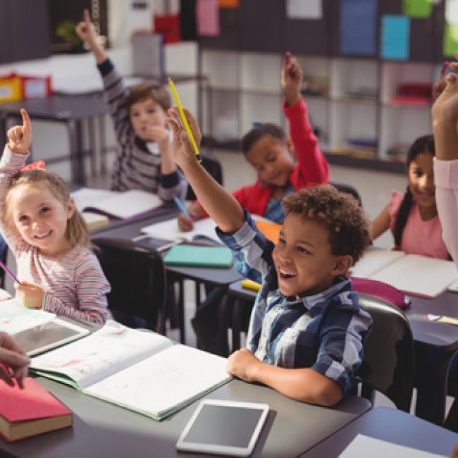 Children in a classroom raising their hands to answer a question