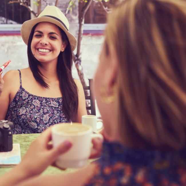 Woman vaping with e-cigarette at a table with another woman drinking coffee.