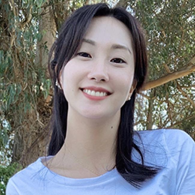 Dr. Ye Ji Kim, a dark-haired Korean American female-identifying epidemiologist wearing a light blue top and standing in front of a tree 