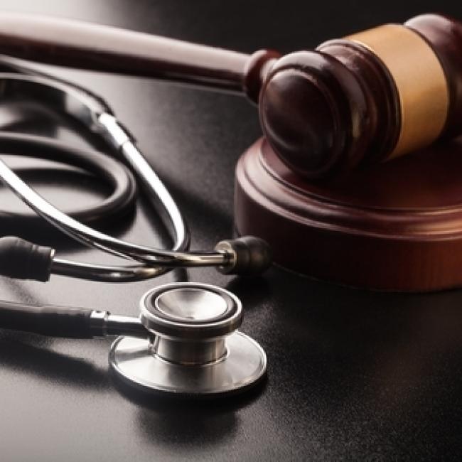 Silver and black stethoscope placed next to a wooden gavel 