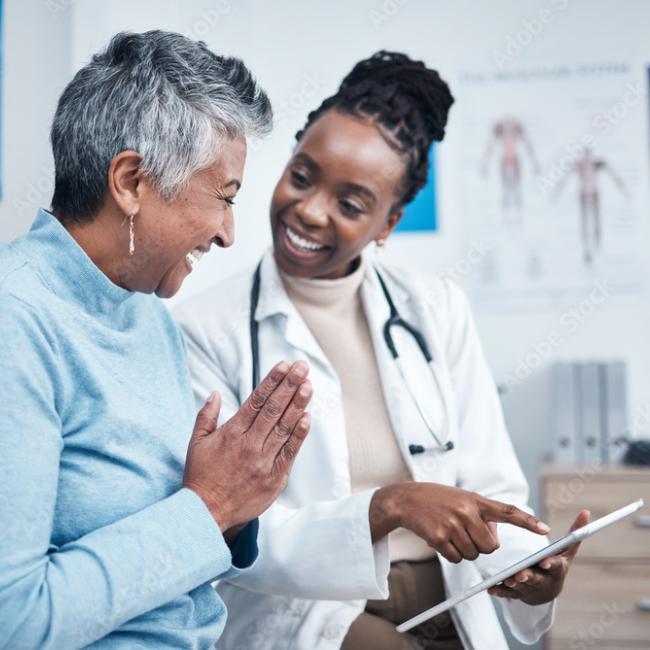 Black doctor smiling and holding a clipboard to help an elderly patient