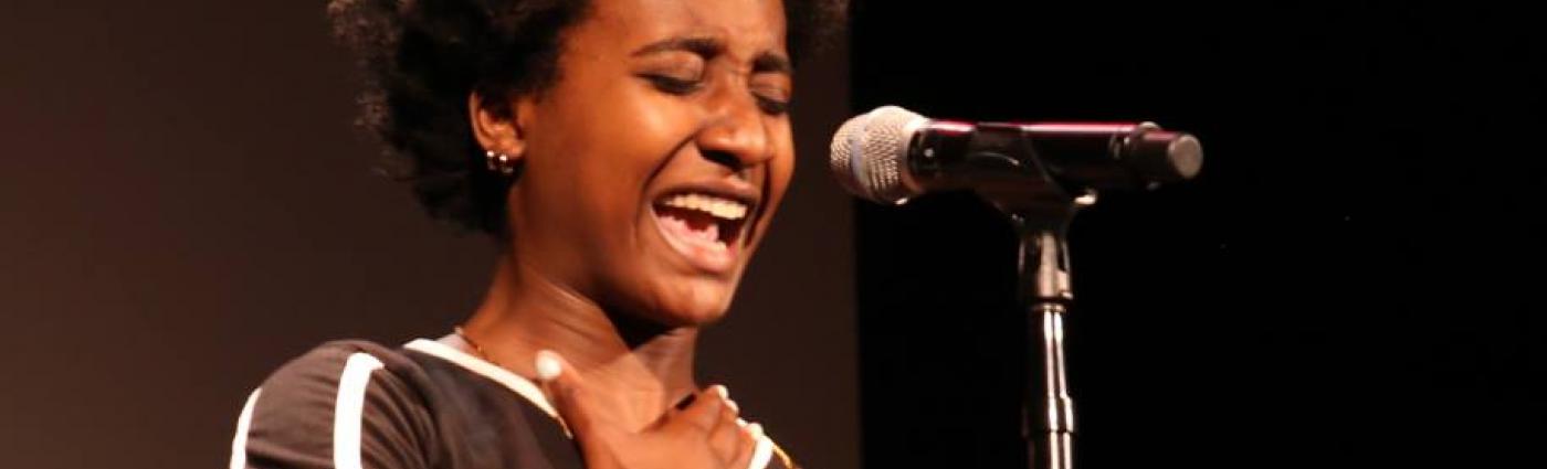Young African American woman passionately speaking into a microphone on stage.