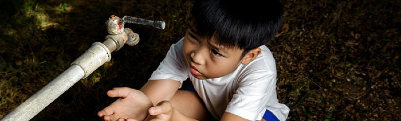 Image of a boy with his hands cupped under a spigot.
