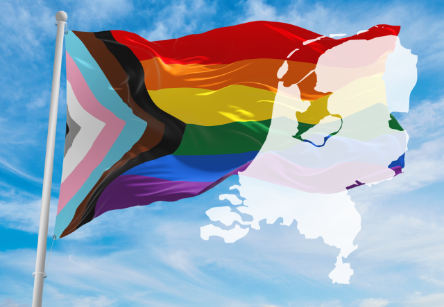 PRIDE flag rippling in the wind in front of a blue sky with wispy white clouds and a map of the Netherlands superimposed over it
