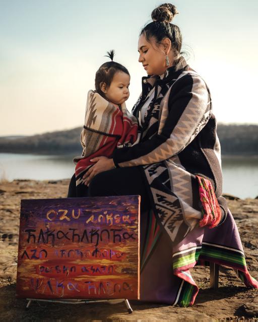 Indigenous mother and child with a sign that reads, "you feel empty  because you were mistreated yet you are held sacred , no one cries alone around me"