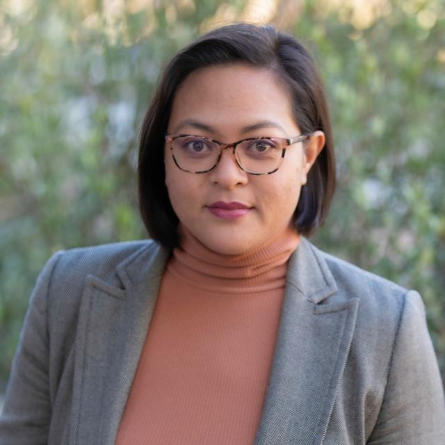 Dr. Charisse Iglesias, a woman with short, dark hair wearing glasses and a grey blazer with a peach colored top