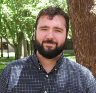 Dakota Cintron: smiling man with dark hair and a full beard and mustache wearing a blue checkered shirt